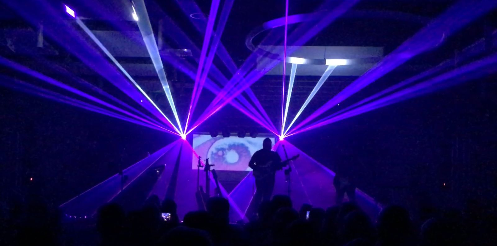 A guitarist on stage under purple and blue lasers, in front of the crowd
